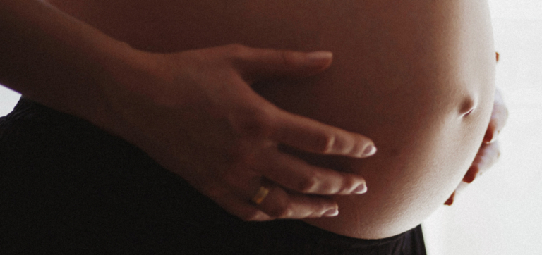 Close-up of hands gently holding a pregnant belly.