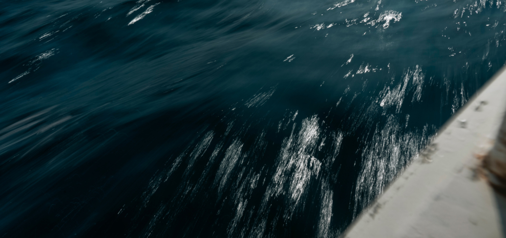 Dark ocean water with sunlight reflections beside a boat railing